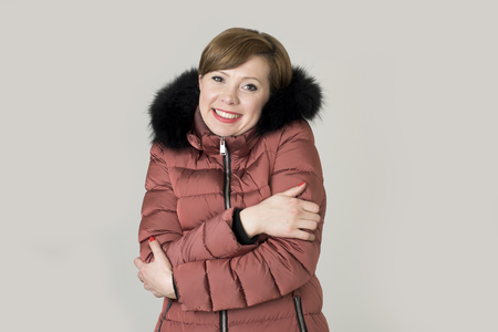 young read hair attractive and sweet woman 20s or 30s posing isolated wearing warm winter jacket with fur hood shivering and freezing feeling cold in sweet face expressionの写真素材