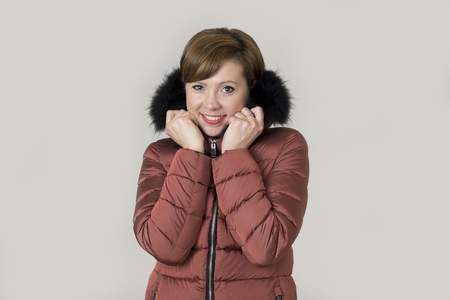 young attractive and happy red hair Caucasian woman on her 20s or 30s posing cheerful and smiling wearing warm winter jacket with fur hood isolated on grey background in seasonal fashion conceptの写真素材