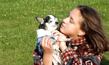 Girl in a bright sweater playing with a small dogの写真素材