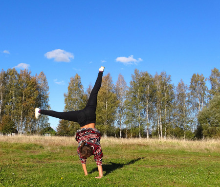 Girl on the grass on a Sunny day tumbling gymnastic exercises doing