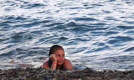 The girl lies on the shore of a calm sea in the waterの写真素材