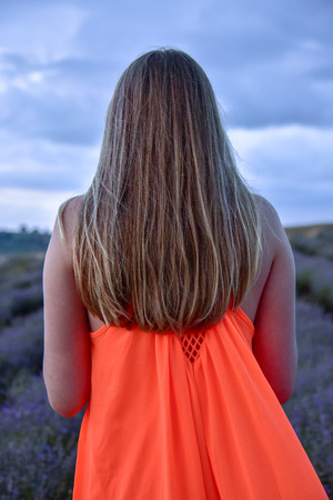 Girl standing on the road in the field at dawn in a bright orange dress on a pale background, romantic thoughtfully young beautifulの写真素材