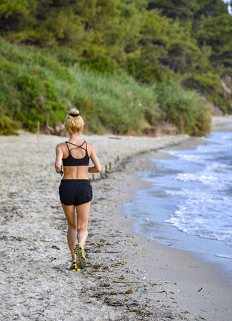 Sporty girl in black swimsuit runs along the sea in summer morning jog back to the cameraの写真素材