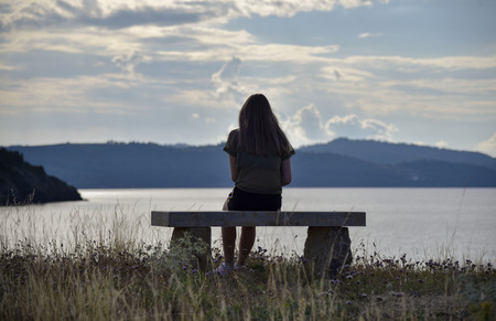 girl sitting on a bench near the sea and looking into the distanceの写真素材