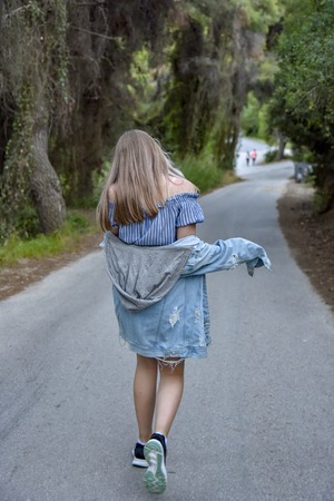 Tourist girl in denim clothes walking on the road in the woodsの写真素材