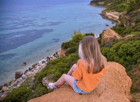 Girl in an orange jacket sitting on a cliff above the seaの写真素材