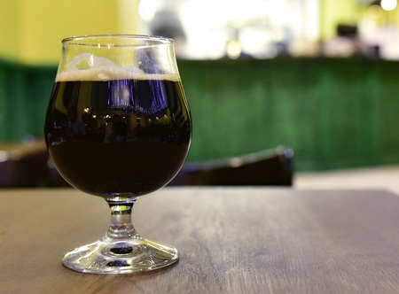 A glass of dark beer on the bar table. Green yellow backgroundの写真素材