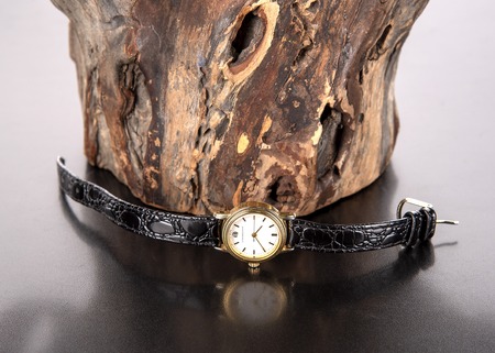 Wrist watch with gold dial and black leather strap on wood backgroundの写真素材