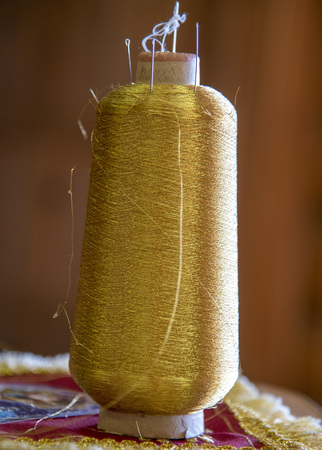 A coil of gold thread stands on the table. The coil is inserted the needle.の写真素材