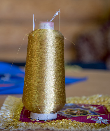 A coil of gold thread stands on the table. The coil is inserted the needle.の写真素材
