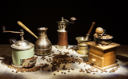The photo was taken in the technique of "Light brush". Mini-collection.On the table are coffee grinders, Turk and mortar.Coffee beans are scattered around.の写真素材