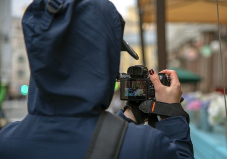 Girl-photographer takes photos of veranda outdoor cafe on the streets of the city.The photo was taken from the back, on the camera screen you can see a preview.の写真素材