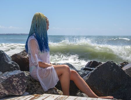 A girl with blue Senegalese pigtails is sitting on the stones.の写真素材