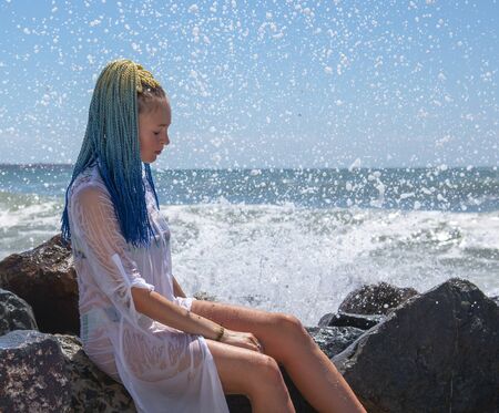 A girl with blue Senegalese pigtails is sitting on the stones.の写真素材