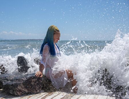 A girl with blue Senegalese pigtails is sitting on the stones.の写真素材