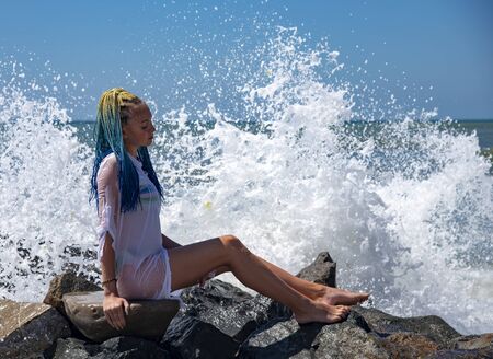 A girl with blue Senegalese pigtails is sitting on the stones.の写真素材
