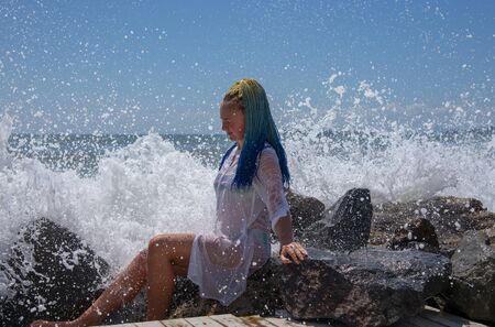 A girl with blue Senegalese pigtails is sitting on the stones.の写真素材