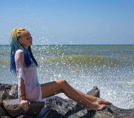 A girl with blue Senegalese pigtails is sitting on the stones.の写真素材