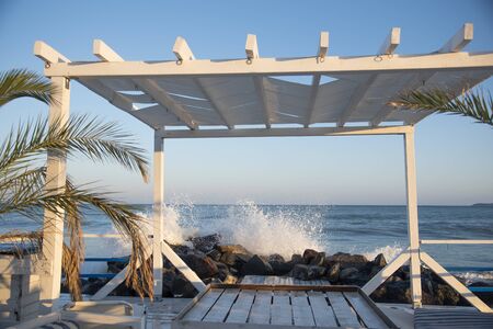 White wooden veranda on the beach.In the background, the waves break on the rocks and spray scatter in different directions.の写真素材