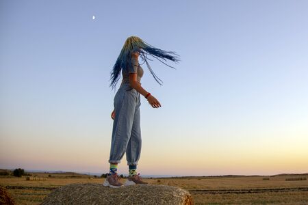 The girl with the blue braids Senegalese standing on a haystack at sunset sky background.She turns and braids undress in different directions.の写真素材
