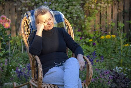 An elderly woman rests in a wicker chair in her garden.Illuminated by the evening sunlight.の写真素材