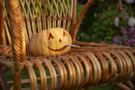 Smoking Halloween pumpkin sitting in a wicker chairの写真素材