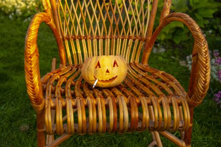 Smoking Halloween pumpkin sitting in a wicker chairの写真素材