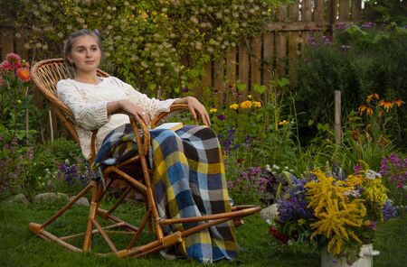 Beautiful girl sitting in a wicker rocking chair with a bookの写真素材