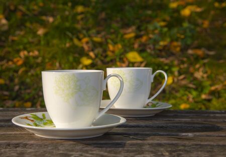Two cups of tea stand on a wooden surface, against the background of autumn leaves.の写真素材