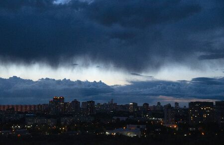 Background.Dark gloomy ragged clouds over the evening city. The city lights up the Windows and lanterns.の写真素材