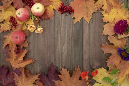 Frame of bright autumn leaves, berries, apples and flowers on a wooden background. Free space for insertion.の写真素材