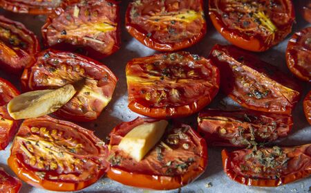 Freshly cooked sun-dried tomatoes, sprinkled with spices and drizzled with oil are laid on parchment . Between them cloves garlic.の写真素材