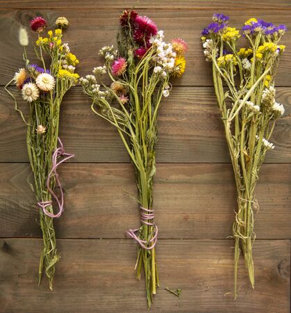 Three bright colorful bouquets of dried flowers on a wooden background.の写真素材