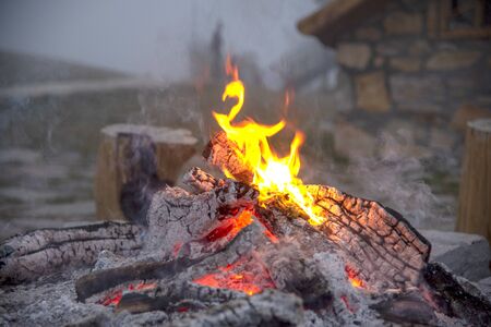 The dying fire, wood, coals and ashes.Thick smoke over the fire, in the background the stone wall of...