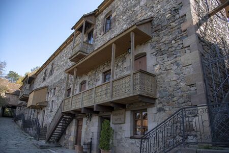 A fragment of a house with a balcony with a carved railing of dark wood and a tiled roof.