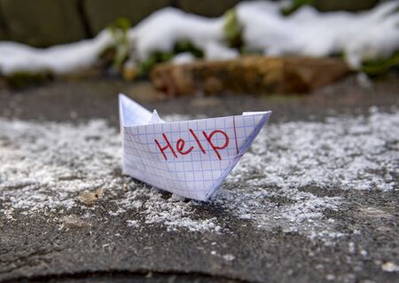 A paper boat made of a checkered notebook with the inscription help stuck in the ice.