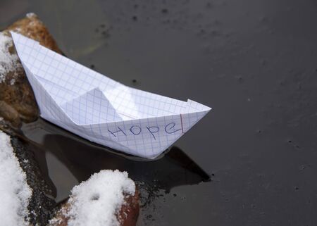 A paper boat made of a checkered notebook with the inscription HOPE stuck in the ice.