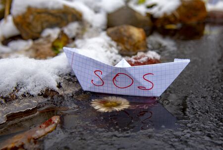 A paper boat with the inscription SOS stuck in the ice.の写真素材