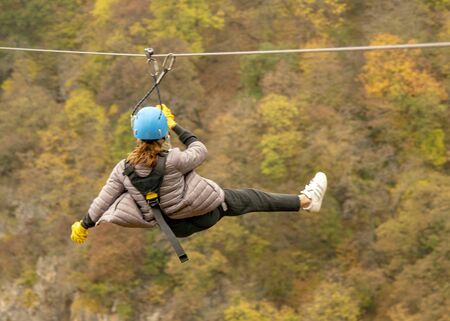 A teenage girl flies on a zipline against the background of mountains covered with autumn forest.のeditorial素材