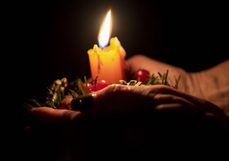 Hands of an elderly woman holding a Christmas candle. on dark background.の写真素材