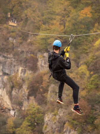 Armenia, enokavan, October 2019.A young man in a black tracksuit and special equipment flies on a zip line on the background of the autumn landscape.のeditorial素材