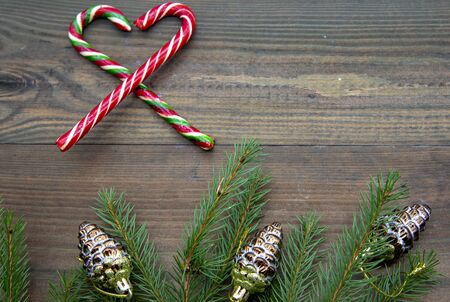 Two Christmas candy folded into a heart and fir branches with glass cones on a wooden background.の写真素材