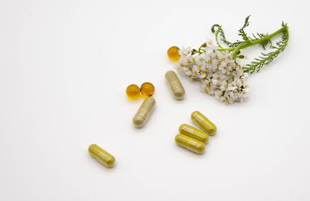 Fresh yarrow flower and various capsules and pills on a light background.の写真素材
