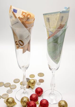 Two glasses with paper euros on a light background. Around Christmas balls and small coins.の写真素材