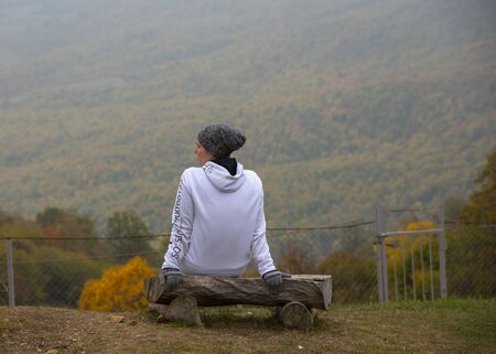 Armenia, enokavan, October 2019. Autumn landscape.The girl sits on a bench on the hillside Fields and mountains stretched before her. A thick fog descends.のeditorial素材