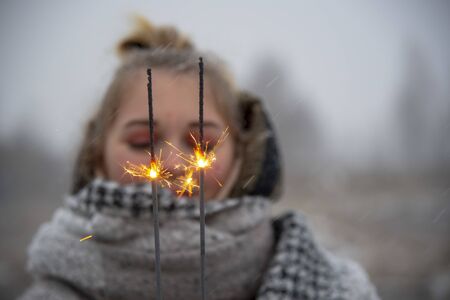 Cheerful burning sparklers on the background of a blurred portrait of a girl in nature.の写真素材