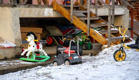 Russia, Moscow region, January 2020. Children's rocking horse, Bicycle and toy car are on the snow at the wall of the house.のeditorial素材