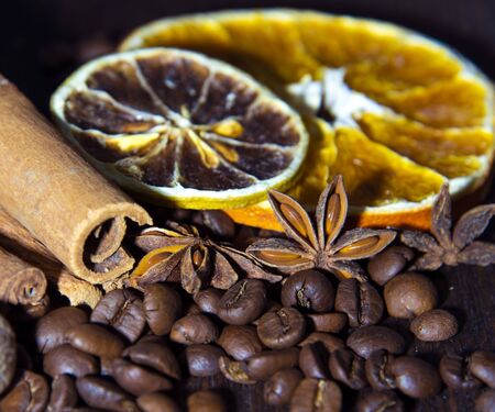 Coffee beans with citrus cinnamon sticks and star anise on wooden surfaces.
