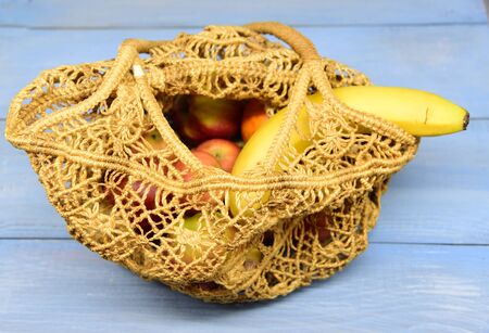 Various fresh fruits in a woven bag made of eco-friendly materials on a blue wooden tabletop.の写真素材