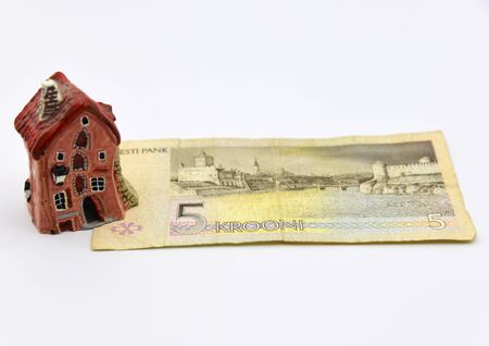 A small ceramic house stands on a disused Estonian five-kroner banknote.An Old paper banknote,...